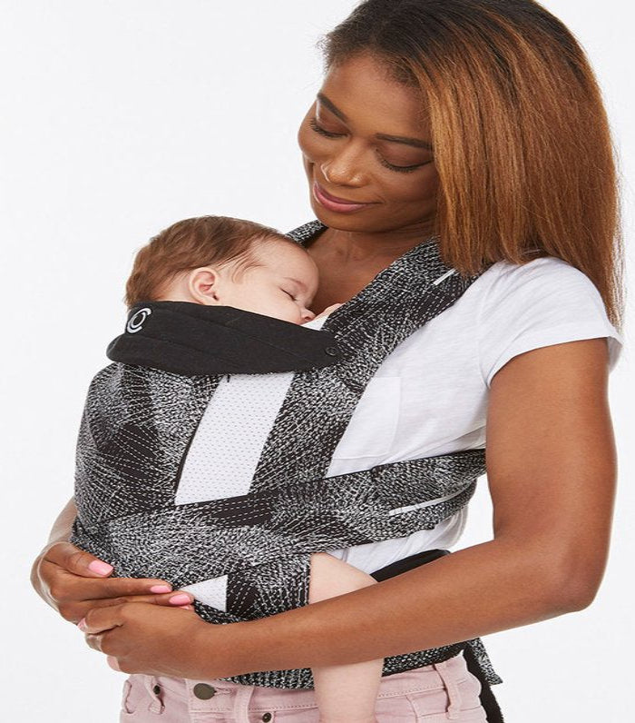 Woman holding a baby in a black and white patterned baby carrier against a white background