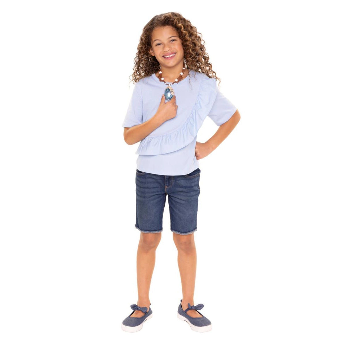 Young girl wearing a light blue top and denim shorts on a white background with a necklace
